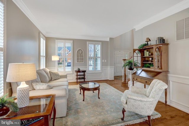 living room featuring crown molding, a decorative wall, wood finished floors, and a wainscoted wall