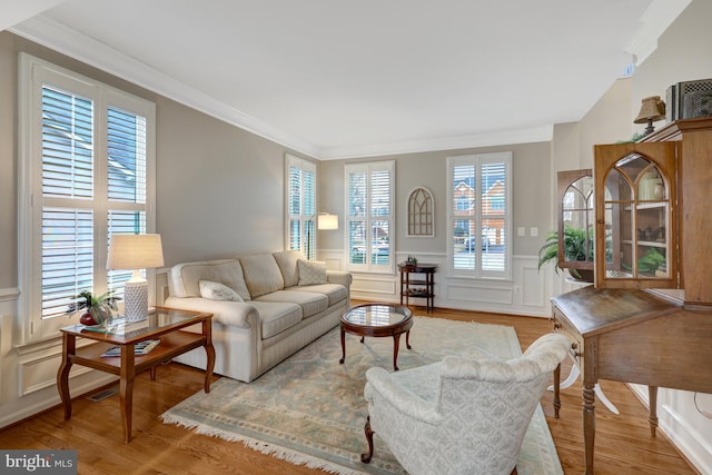 living area with a wainscoted wall, wood finished floors, a decorative wall, and ornamental molding