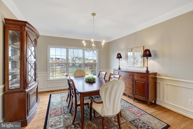 dining area featuring a decorative wall, light wood-style floors, an inviting chandelier, wainscoting, and crown molding