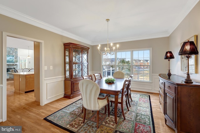 dining room featuring a wainscoted wall, light wood-type flooring, an inviting chandelier, and ornamental molding