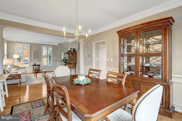 dining space featuring a notable chandelier, a wainscoted wall, light wood-style flooring, and ornamental molding