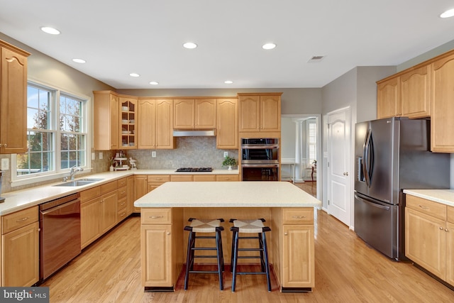 kitchen with light brown cabinets, a breakfast bar, stainless steel appliances, under cabinet range hood, and a center island