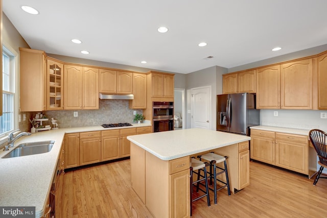 kitchen featuring light brown cabinets, stainless steel appliances, a sink, under cabinet range hood, and a center island