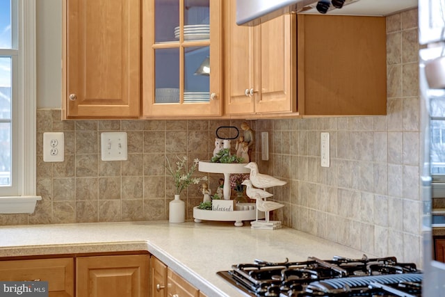 kitchen with glass insert cabinets, gas cooktop, tasteful backsplash, and light countertops