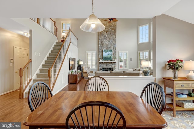 dining space with wood finished floors, a high ceiling, a stone fireplace, baseboards, and stairs