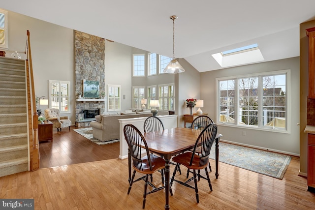 dining area featuring high vaulted ceiling, stairway, light wood-style floors, a skylight, and a fireplace