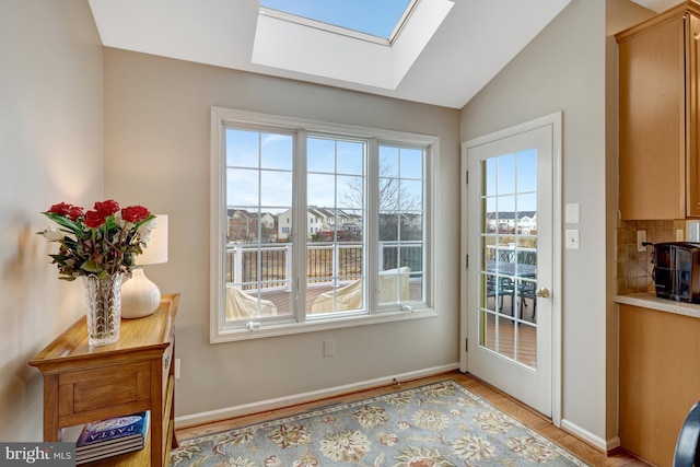 entryway with vaulted ceiling with skylight, plenty of natural light, baseboards, and light wood finished floors