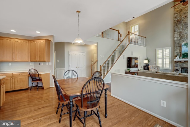 dining space with light wood-style flooring, recessed lighting, stairway, a high ceiling, and a stone fireplace