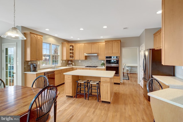 kitchen with a kitchen island, a breakfast bar, light wood-style flooring, light countertops, and appliances with stainless steel finishes