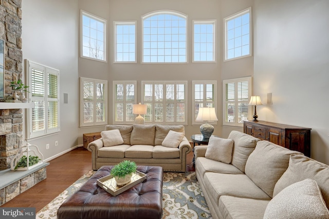 living area featuring baseboards, a stone fireplace, wood finished floors, and a towering ceiling