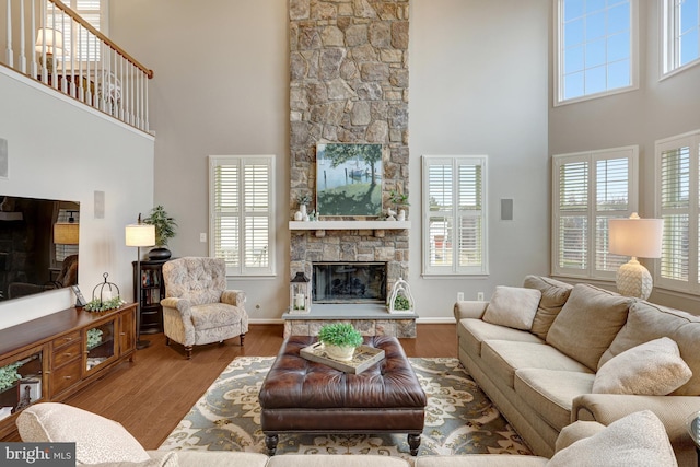 living room featuring baseboards, plenty of natural light, a stone fireplace, and wood finished floors