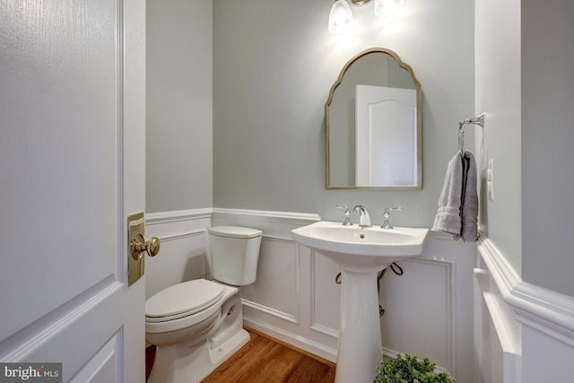 bathroom with a decorative wall, wainscoting, toilet, and wood finished floors