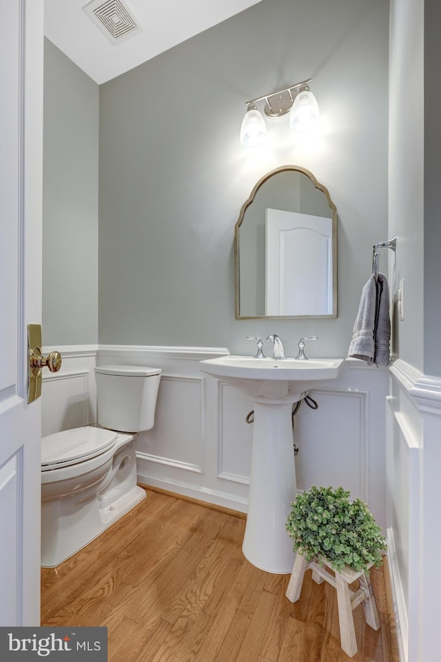 bathroom featuring visible vents, a wainscoted wall, toilet, wood finished floors, and a decorative wall