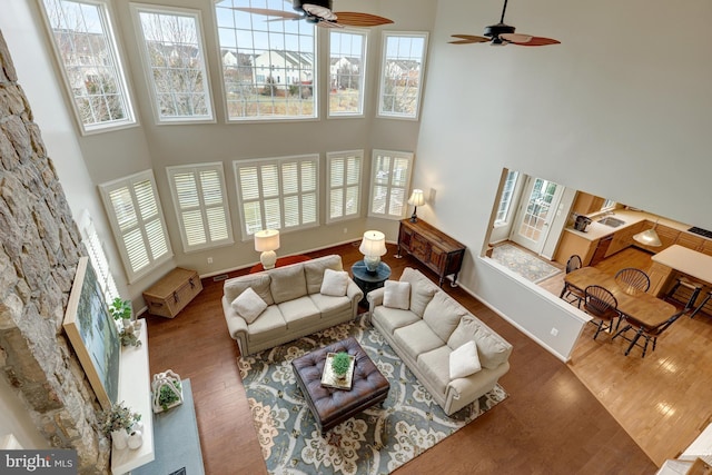 living area with baseboards, a ceiling fan, a towering ceiling, and wood finished floors