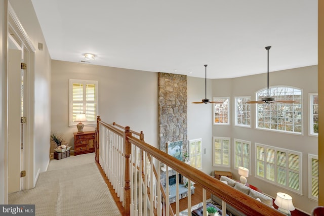 hall with a wealth of natural light, an upstairs landing, and carpet flooring