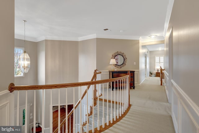 corridor with an upstairs landing, visible vents, a notable chandelier, and ornamental molding