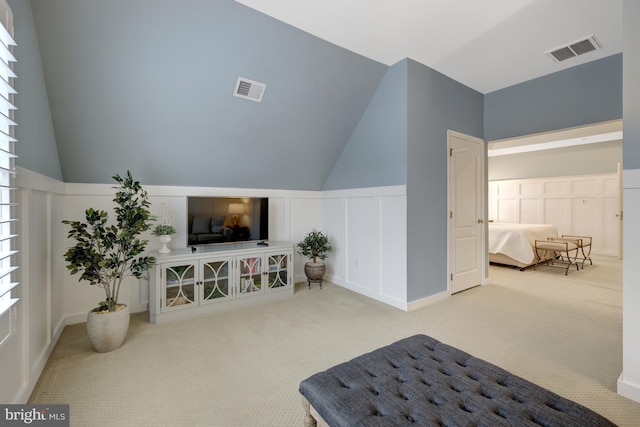 sitting room featuring vaulted ceiling, a decorative wall, visible vents, and carpet floors