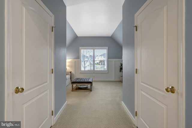 hallway with a wainscoted wall, carpet, and vaulted ceiling