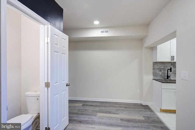 interior space with visible vents, baseboards, light wood-style floors, white cabinetry, and backsplash