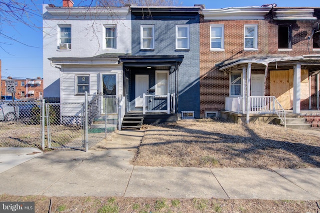 townhome / multi-family property with covered porch, brick siding, and a gate