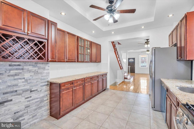 kitchen featuring light tile patterned floors, ceiling fan, stainless steel appliances, light stone countertops, and a tray ceiling