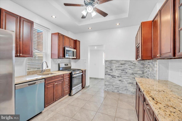 kitchen with a tray ceiling, appliances with stainless steel finishes, a sink, and light stone counters