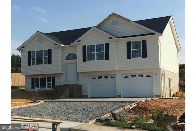 split foyer home featuring an attached garage, driveway, and fence