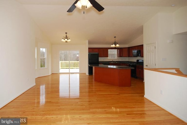kitchen with a center island, light wood finished floors, dark countertops, open floor plan, and black appliances
