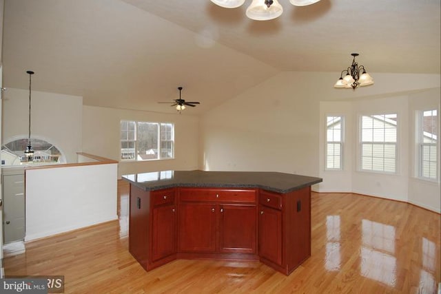 kitchen with reddish brown cabinets, light wood finished floors, dark countertops, vaulted ceiling, and ceiling fan with notable chandelier