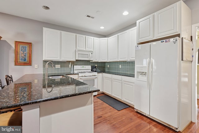 kitchen featuring white appliances, light wood finished floors, white cabinets, a peninsula, and a sink