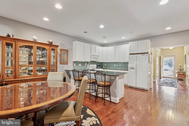 kitchen featuring dark countertops, light wood-style flooring, white cabinets, white appliances, and a peninsula