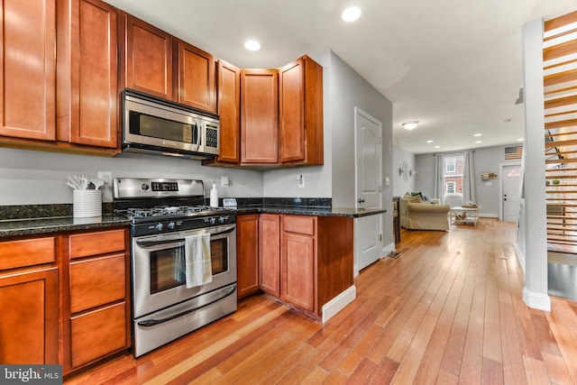 kitchen featuring brown cabinets, light wood-style floors, dark stone counters, and stainless steel appliances