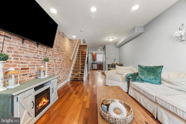 living room featuring recessed lighting, a glass covered fireplace, brick wall, hardwood / wood-style floors, and stairs