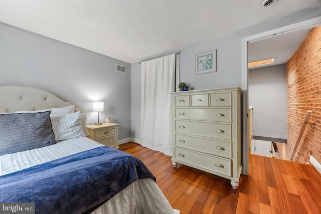 bedroom with brick wall, wood-type flooring, visible vents, and baseboards