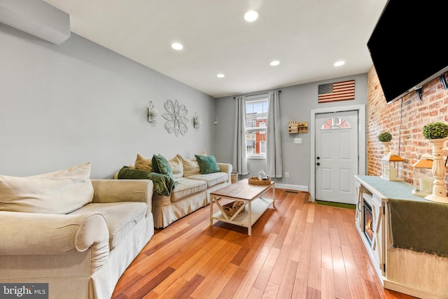 living area with brick wall, light wood-style flooring, baseboards, and recessed lighting