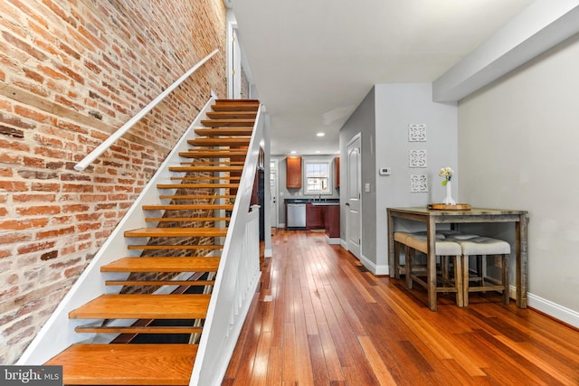 stairs with brick wall, baseboards, and hardwood / wood-style floors