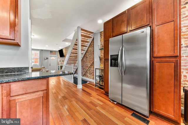 kitchen with visible vents, stainless steel fridge with ice dispenser, brick wall, dark stone countertops, and light wood-type flooring