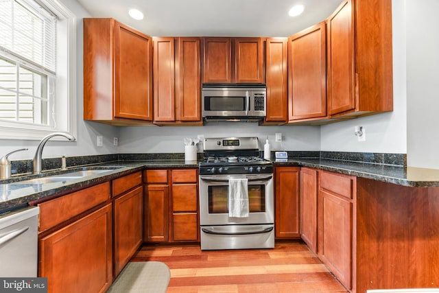 kitchen featuring light wood-style flooring, dark stone countertops, stainless steel appliances, a sink, and recessed lighting