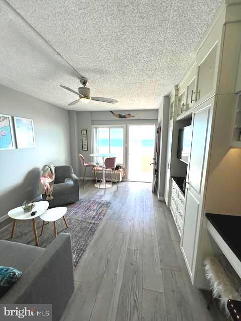 living room with a ceiling fan, wood finished floors, baseboards, and a textured ceiling