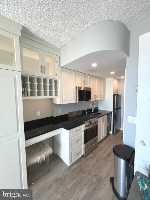 kitchen featuring dark countertops, black appliances, light wood-type flooring, a textured ceiling, and a sink