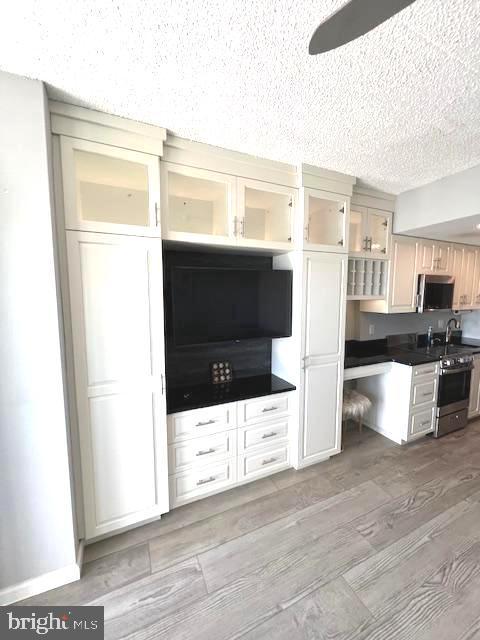 kitchen with light wood-type flooring, a textured ceiling, baseboards, glass insert cabinets, and range