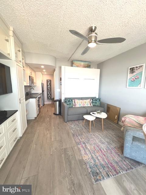 living room featuring a ceiling fan, wood finished floors, and a textured ceiling