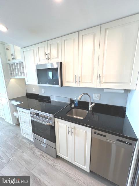 kitchen featuring white cabinetry, dark countertops, appliances with stainless steel finishes, and a sink