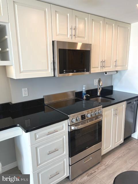 kitchen with a sink, stainless steel appliances, white cabinets, dark countertops, and light wood-type flooring