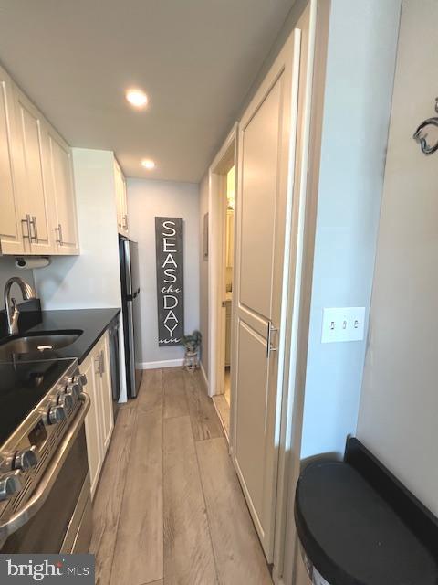 kitchen with light wood-style flooring, stainless steel electric range, freestanding refrigerator, white cabinetry, and a sink