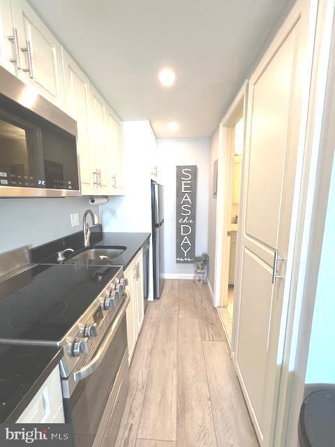 kitchen with dark countertops, baseboards, light wood-type flooring, stainless steel appliances, and a sink