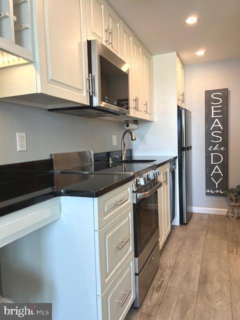 kitchen featuring recessed lighting, light wood-style floors, appliances with stainless steel finishes, white cabinetry, and dark countertops