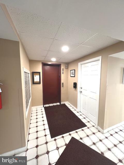 foyer featuring tile patterned floors, elevator, baseboards, and a drop ceiling