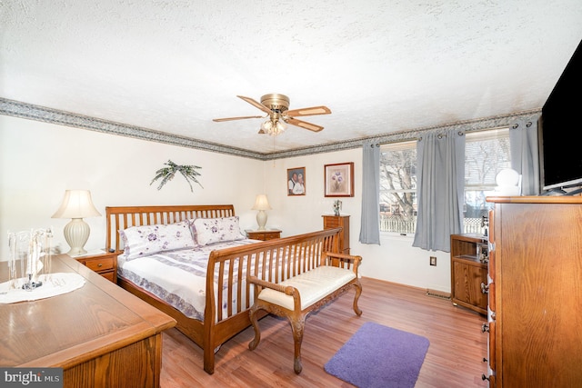 bedroom featuring ceiling fan, crown molding, light wood finished floors, and a textured ceiling