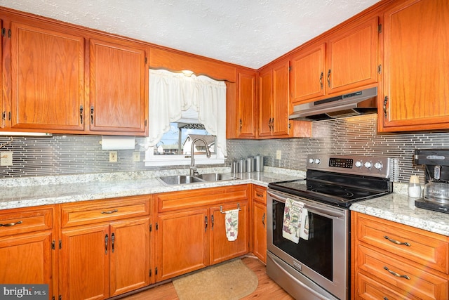 kitchen with under cabinet range hood, brown cabinets, a sink, and electric stove